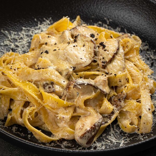 Creamy tagliatelle pasta with mushrooms and cheese served on a dark plate with rustic elegant styling